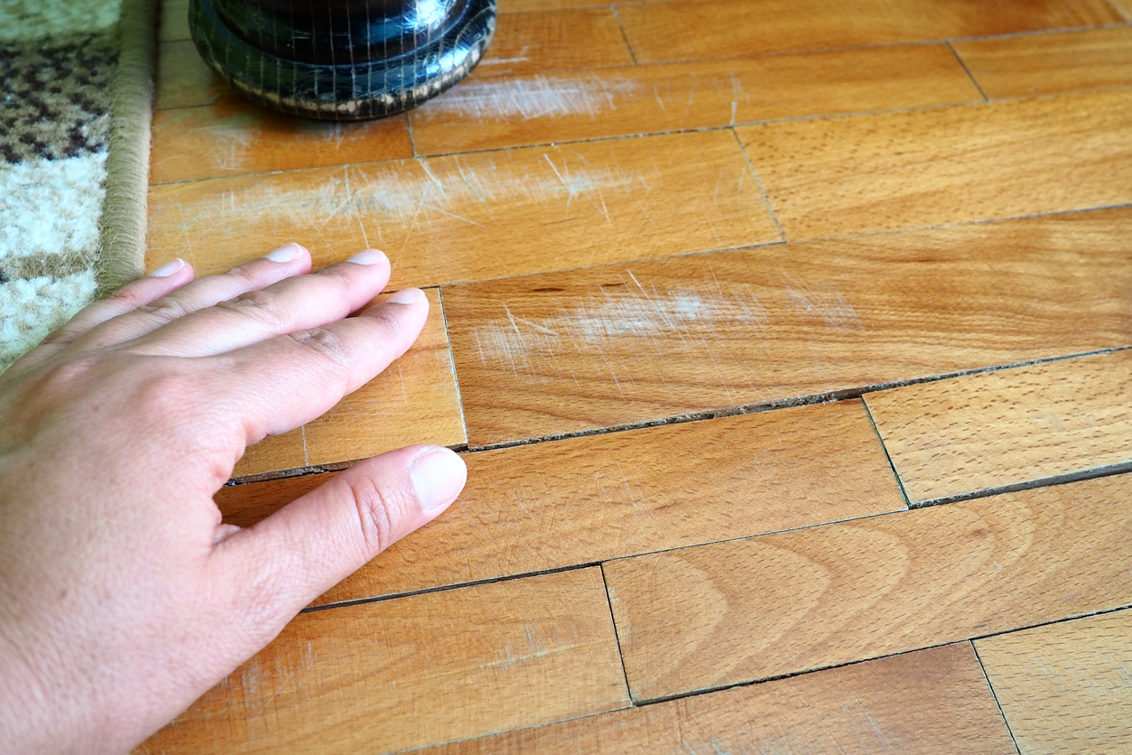 A hand inspecting the scratched up floor where a table leg rested.
